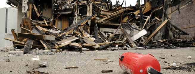 von einem Brand zerstörtes Haus, im Vordergrund ein Feuerlöscher